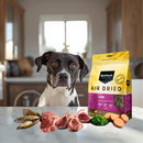 Black Hawk air-dried lamb dog food packaging on a table featuring raw ingredients and a dog with brown eyes