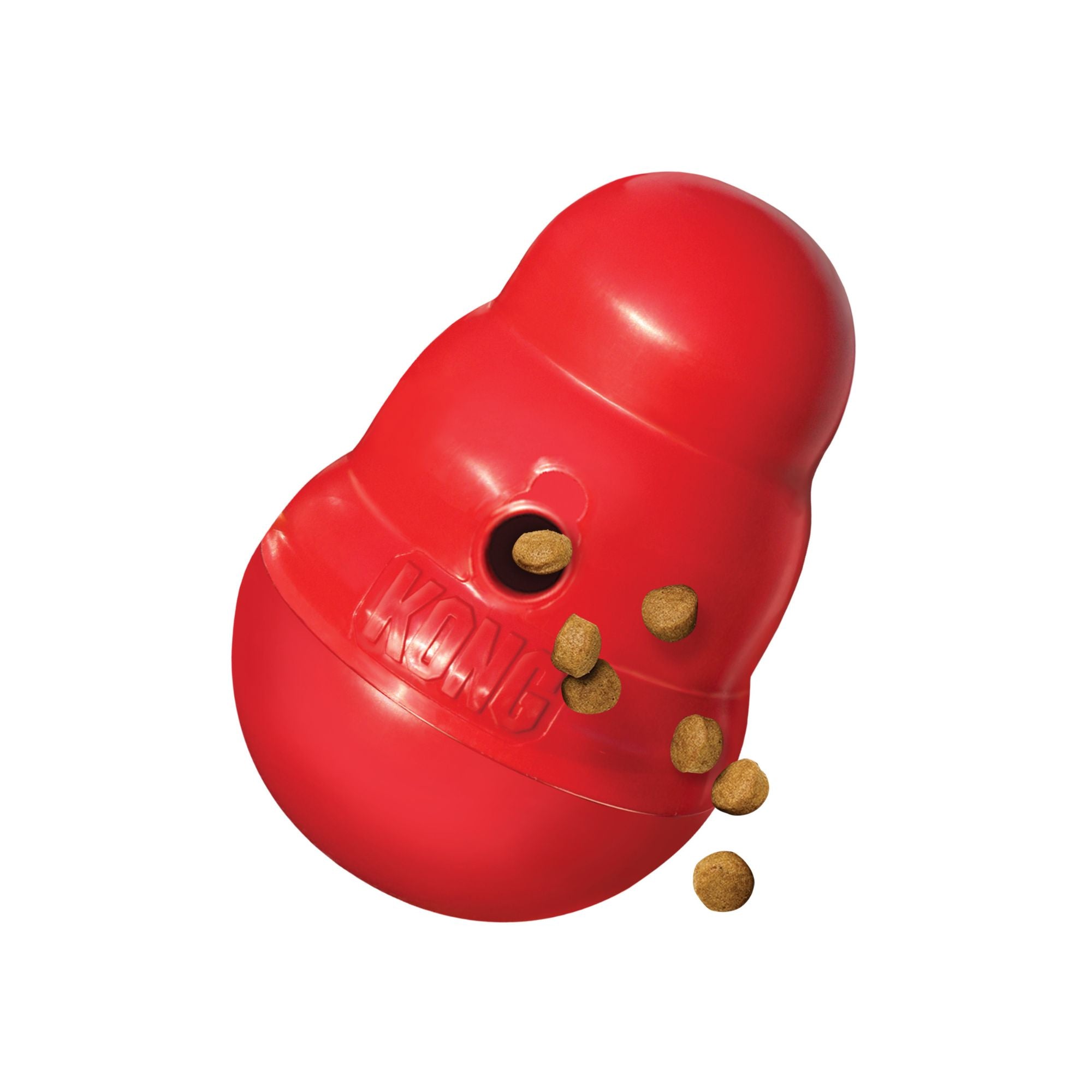 A red KONG Wobbler Dog Treat Dispenser with several brown kibble pieces falling out of its hole, shown on a solid white background.