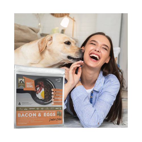 Meals for Mutts Bacon and Eggs adult dry dog food bag next to a relaxed dog and lady