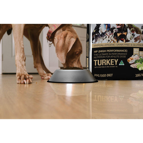 Meals for Mutts High Performance Turkey adult dry dog food bag beside a dog eating out of a bowl