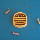 ZippyPaws Happy Bowl Hamburger slow feed dog bowl filled with kibble, styled with dog treats scattered around it.