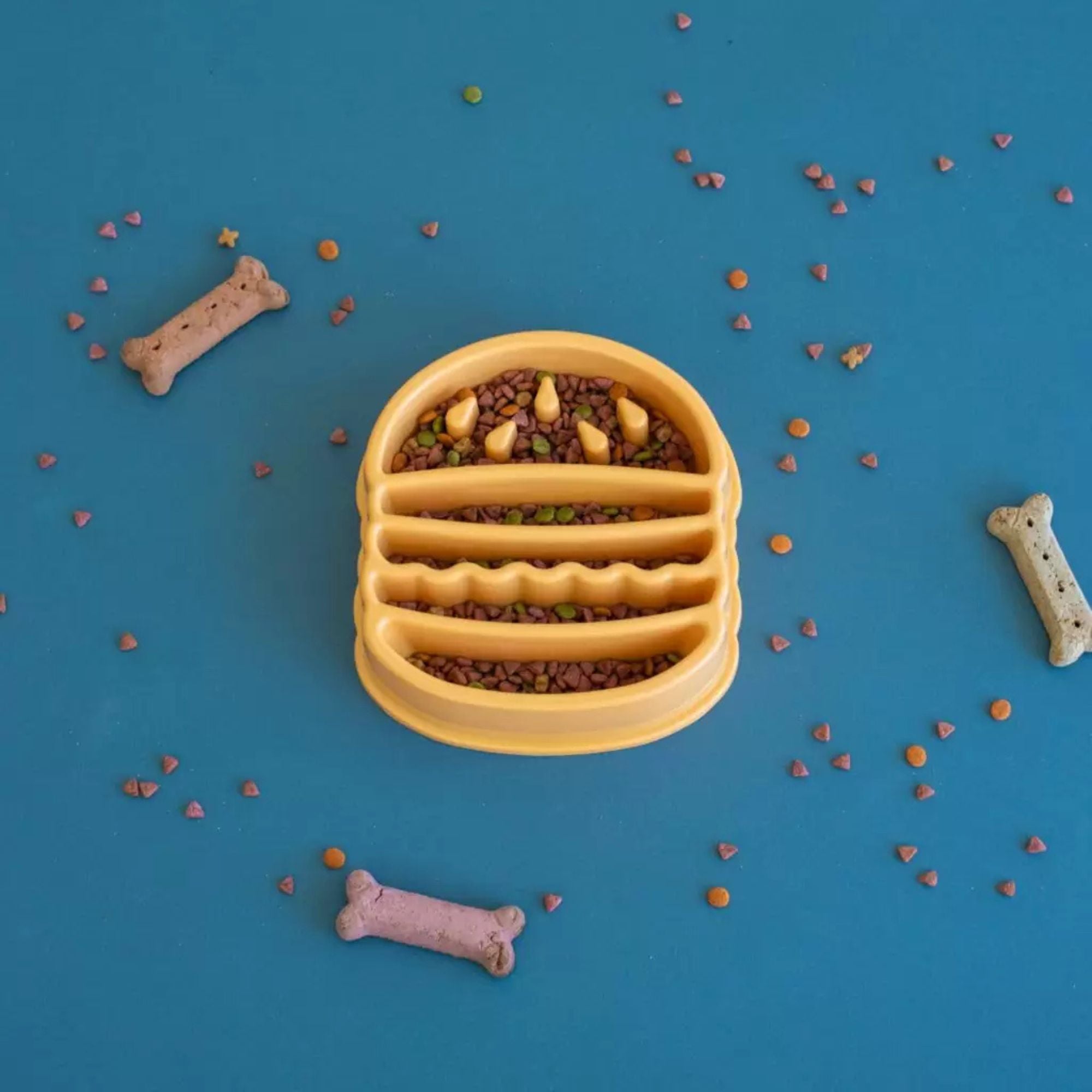 ZippyPaws Happy Bowl Hamburger slow feed dog bowl filled with kibble, styled with dog treats scattered around it.