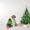 Small white dog sitting beside the ZippyPaws Holiday Burrow Christmas Tree dog toy in a festive room with a decorated Christmas tree and gifts