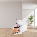 A white dog lies on a light wood floor in a bright room, holding a ZippyPaws NomNomz Boba Milk Tea Plush Dog Toy with a black lid and pink straw. The cup has cute embroidered facial features.